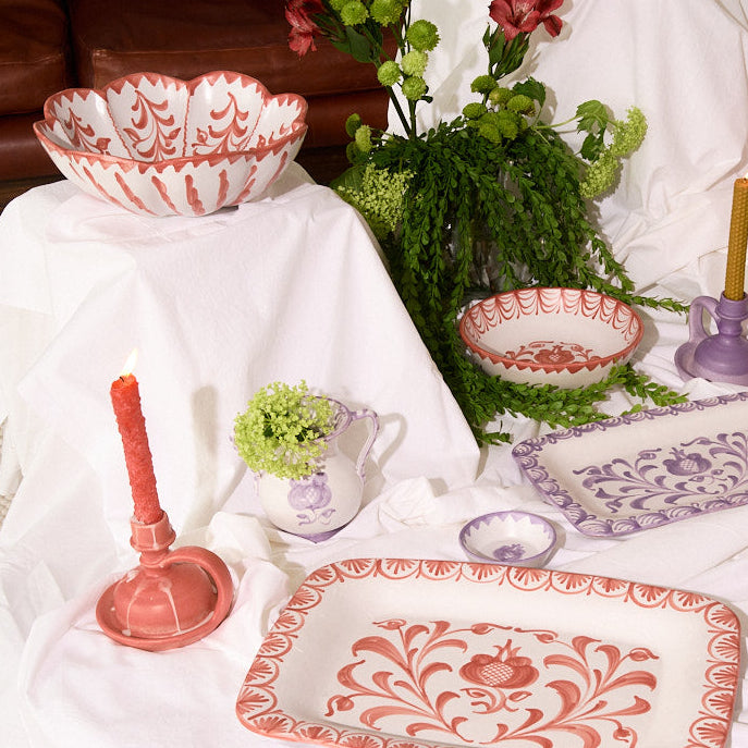 Decorative table setting with patterned plates, candles, and plants on a white tablecloth. - lifestyle