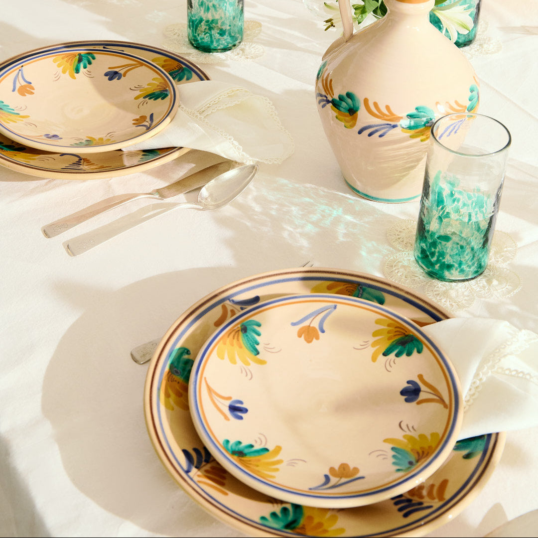 Decorative table setting with floral-patterned plates and vases on a white tablecloth.