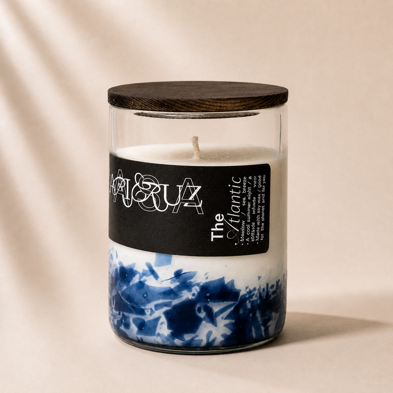 Candle in a glass jar with a black lid and blue and white patterned base on a beige background