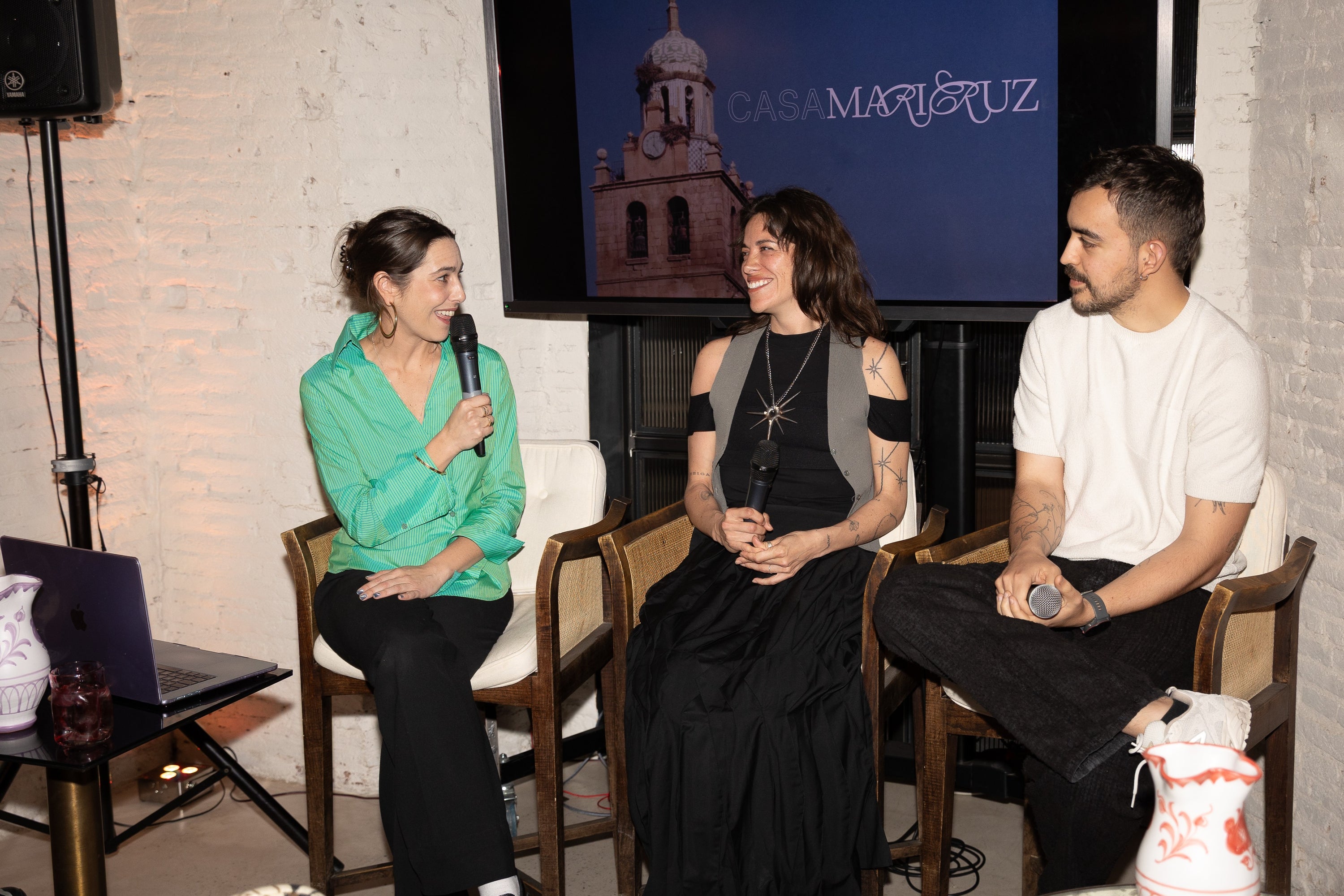 Three people sitting on chairs in front of a screen displaying 'Casa Manzur'.