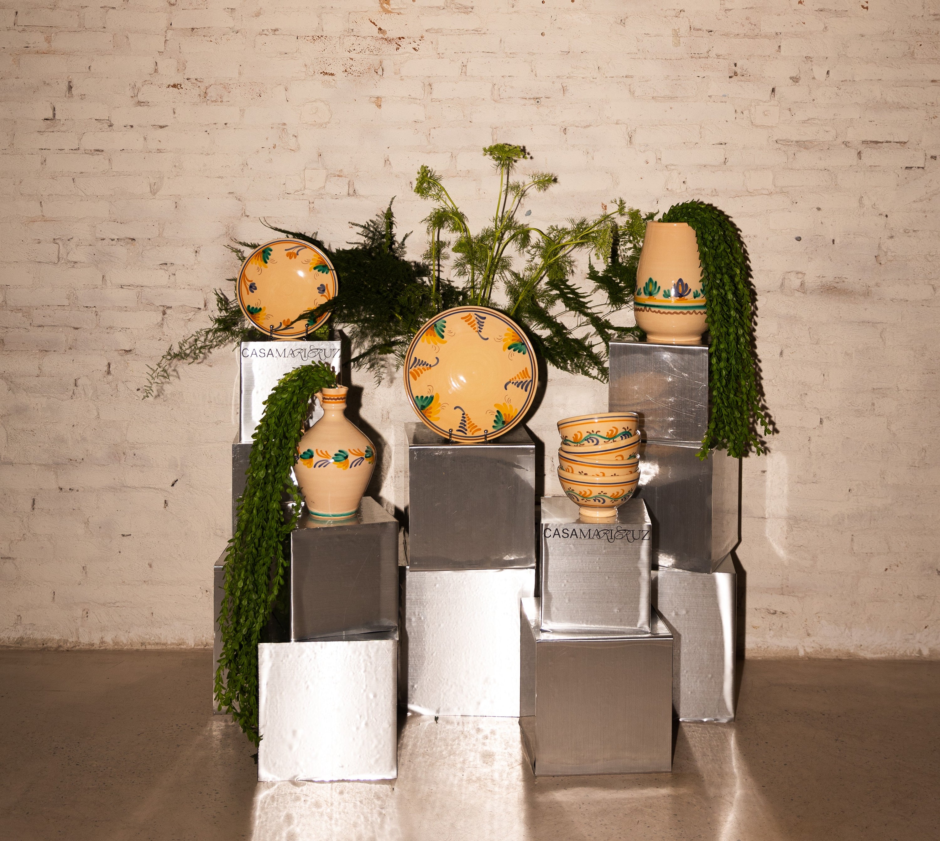 Decorative display of ceramic plates and vases with greenery against a brick wall.
