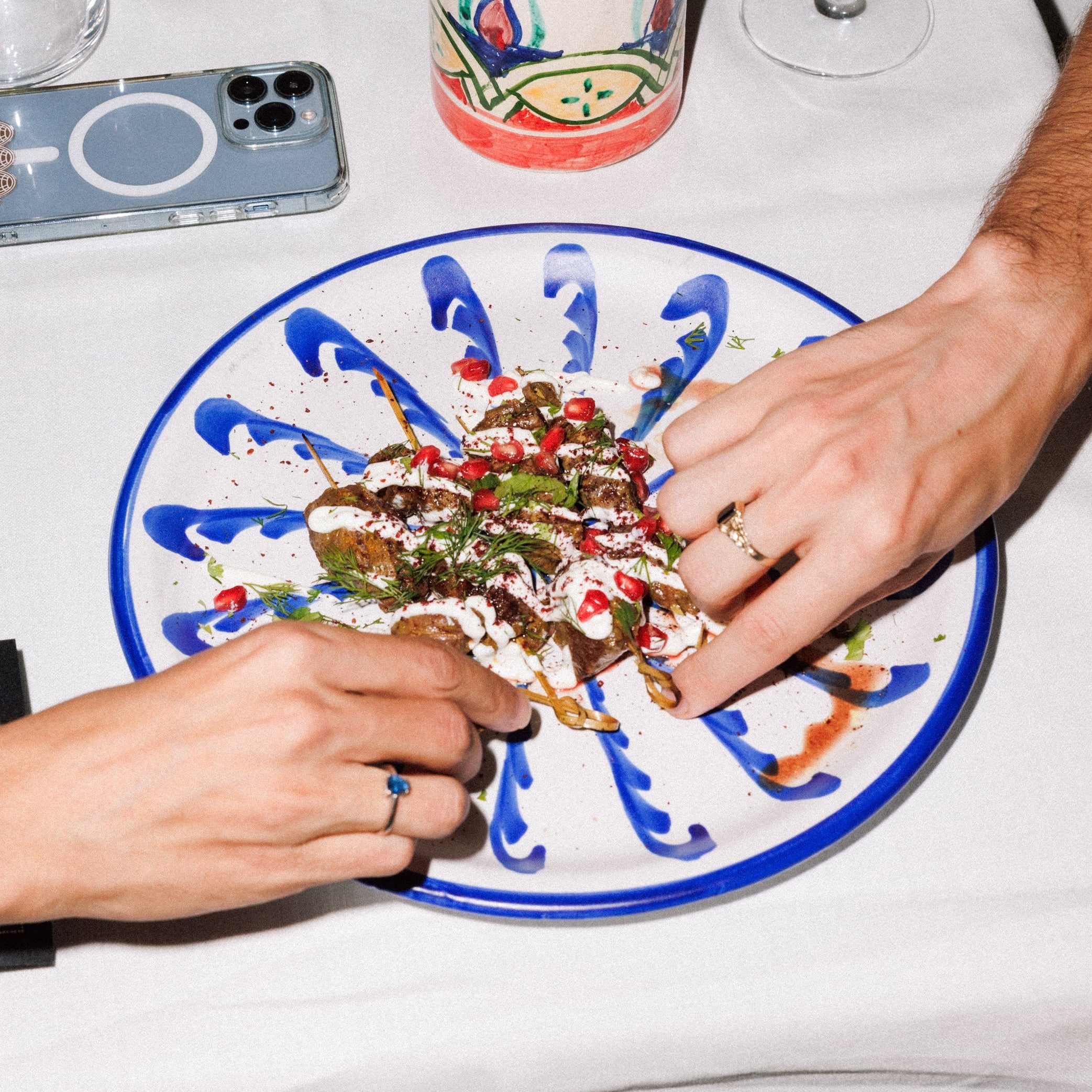 Two hands reaching towards a plate of food on a table with a phone and cup in the background. - lifestyle