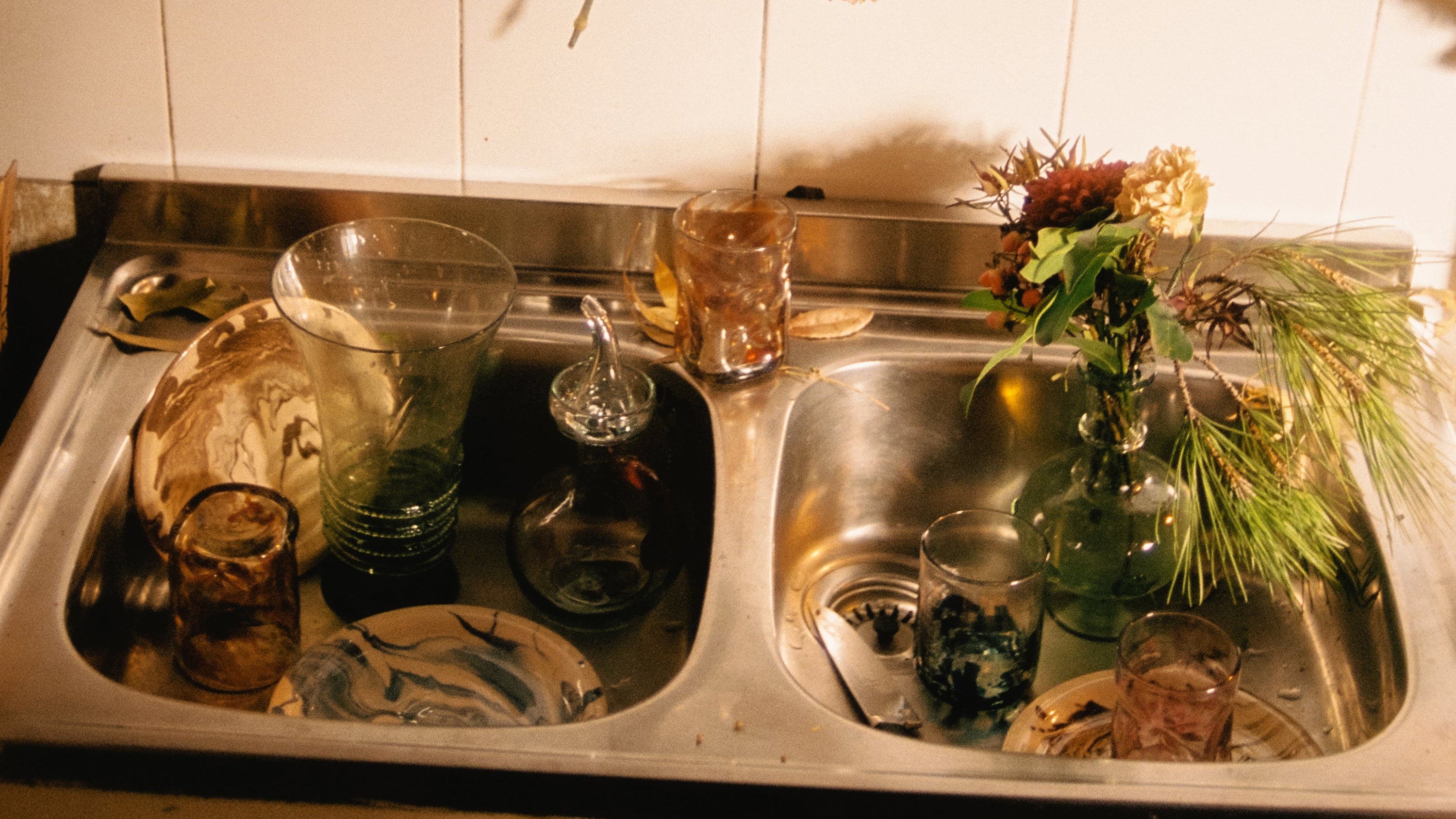 Dirty dishes in a kitchen sink with a tiled wall background