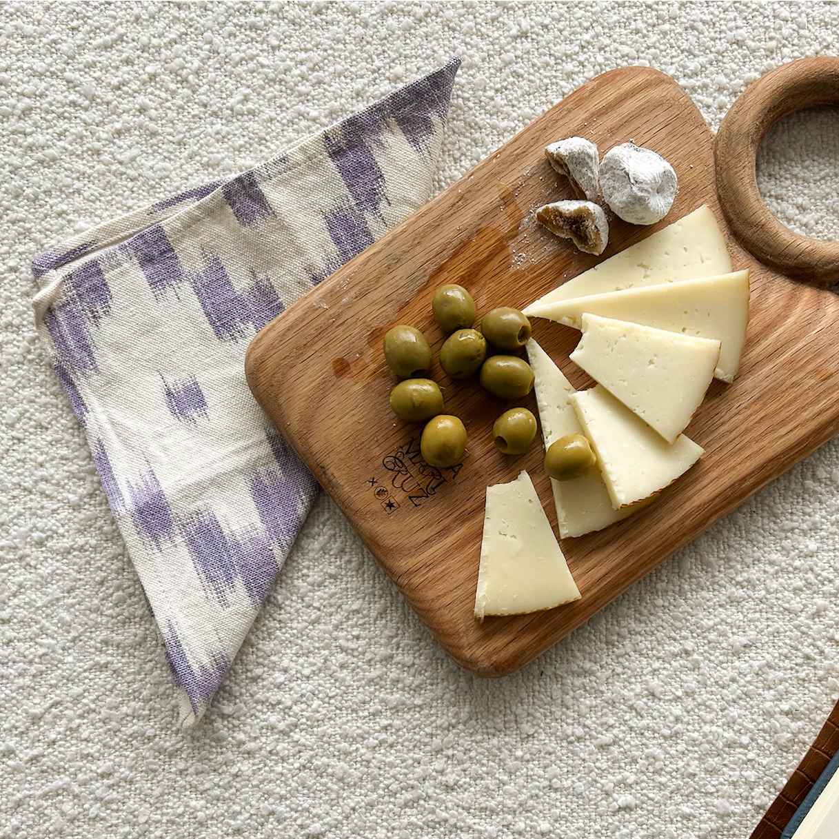 Wooden cutting board with cheese, olives, and nuts on a textured surface. - lifestyle