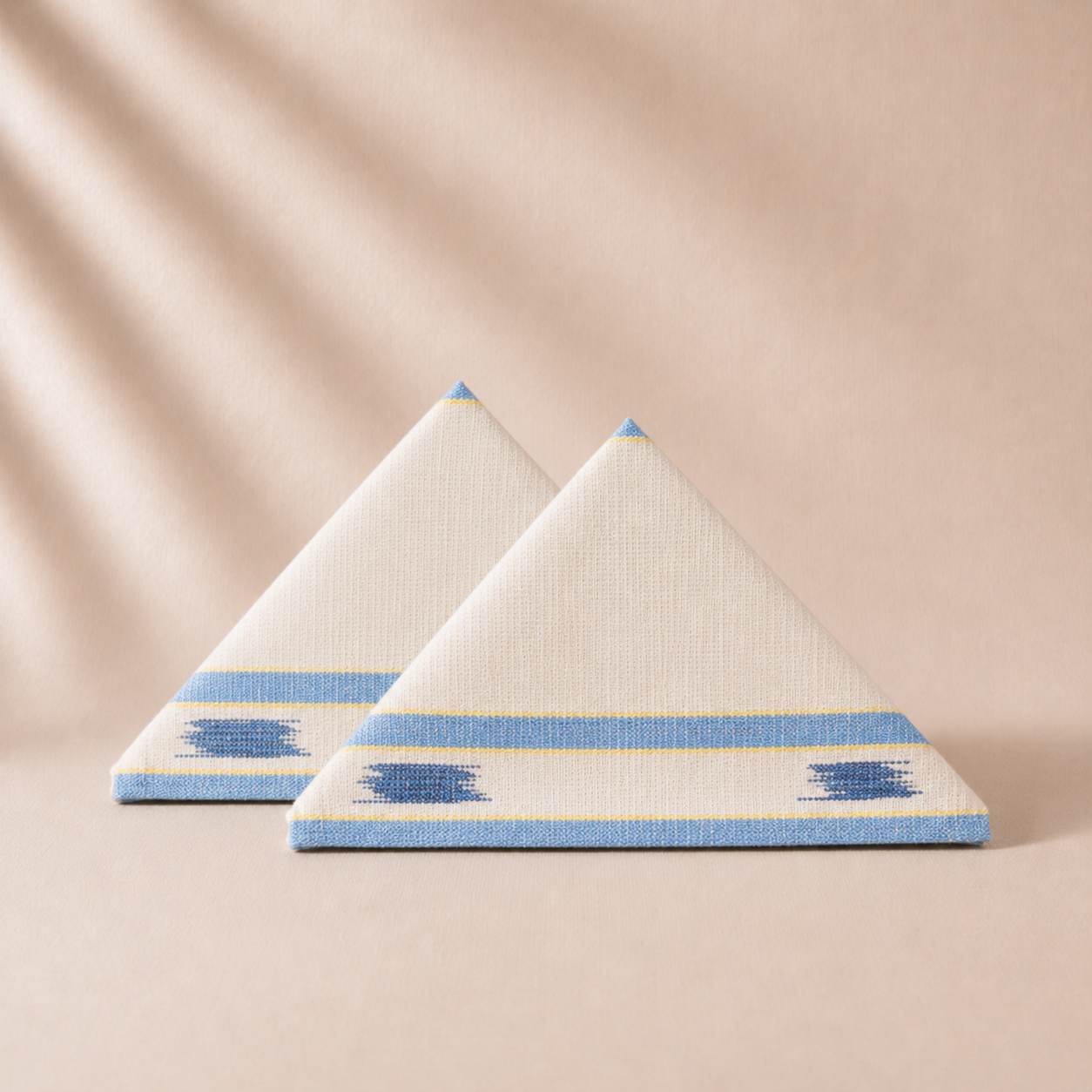 Two triangular napkins with blue and yellow patterns on a beige background