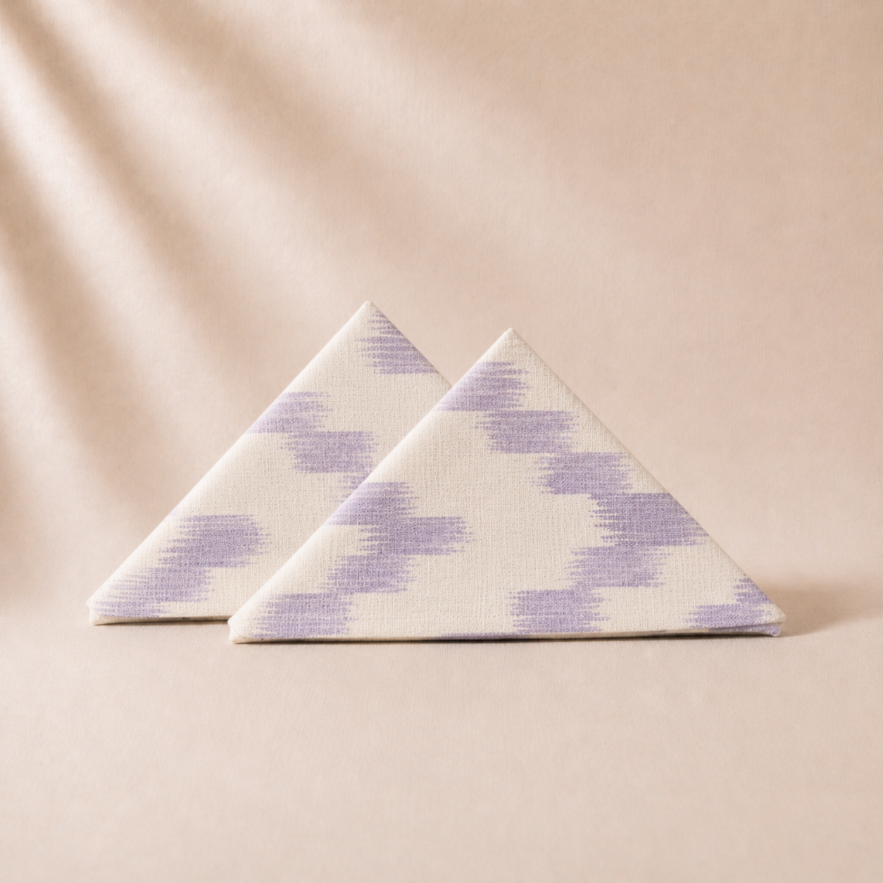 Two triangular napkins with a purple pattern on a beige background