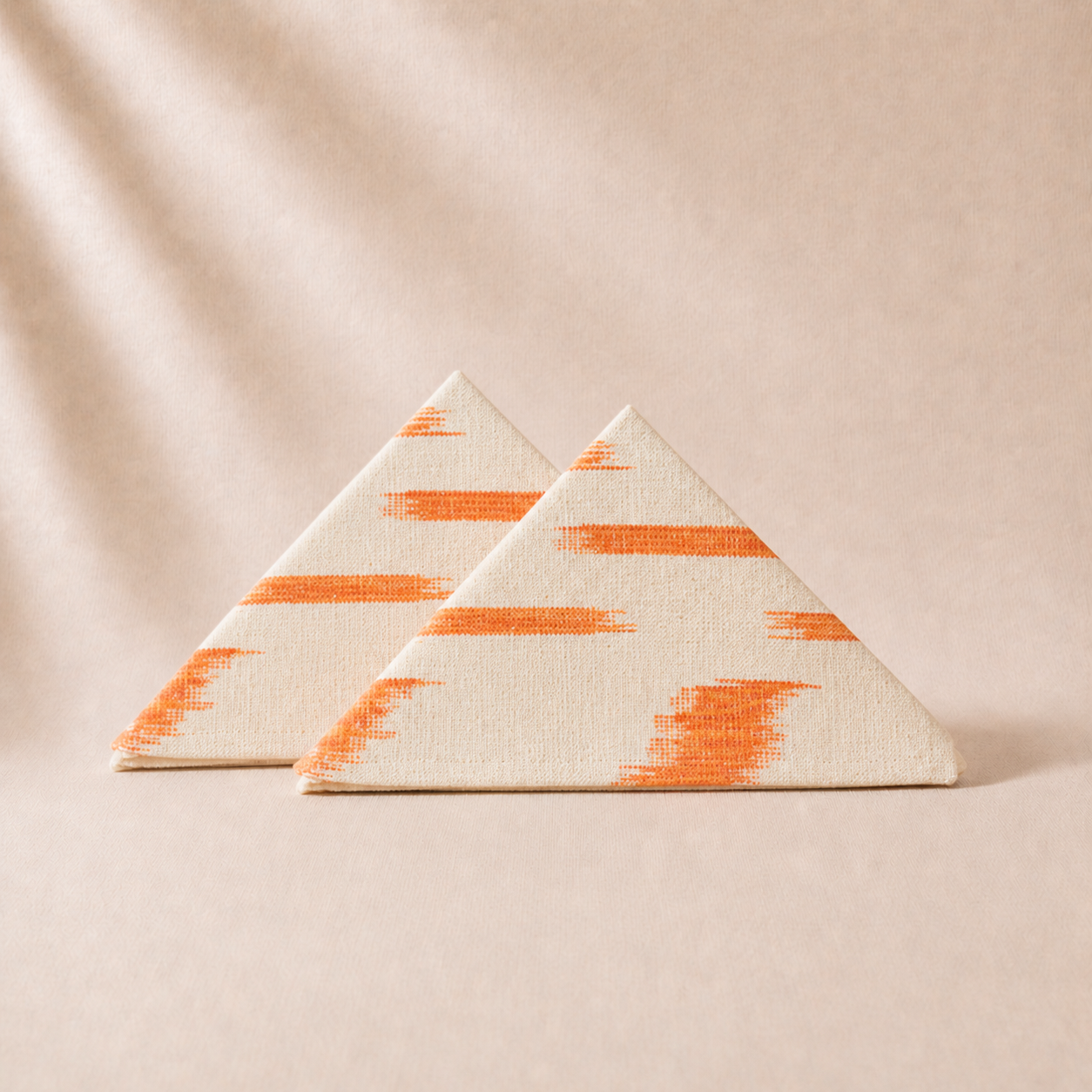 Two triangular fabric pieces with orange and beige pattern on a beige background