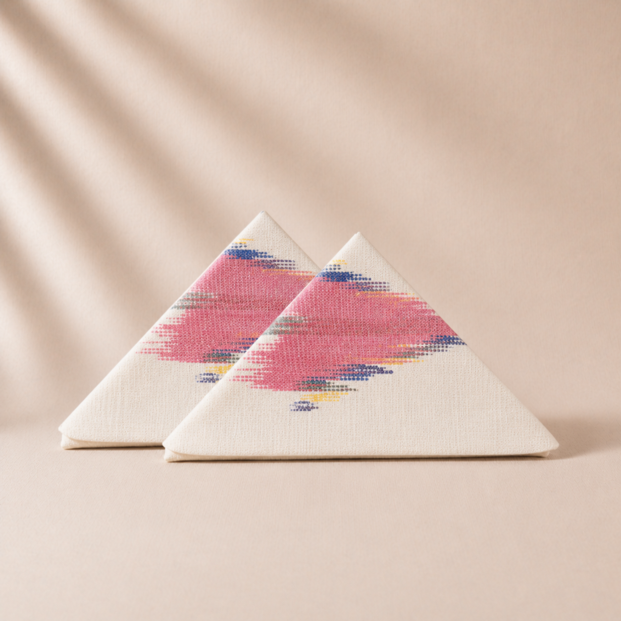 Two triangular napkin pieces with a colorful pink  pattern on a beige background