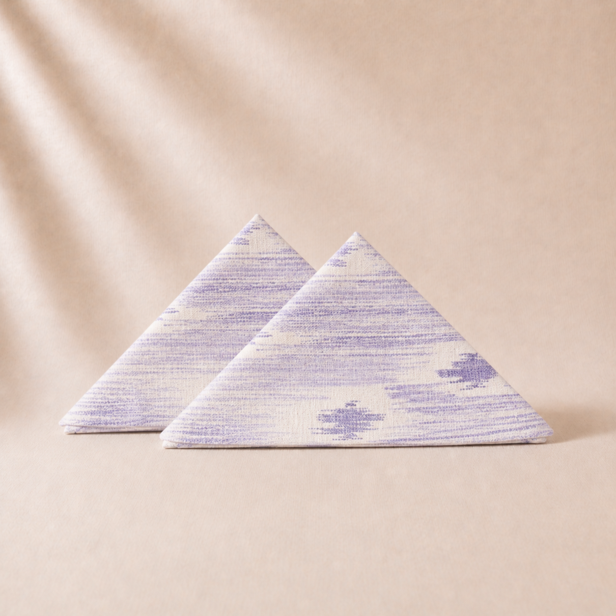 Two triangular fabric napkins with a subtle pattern on a beige background