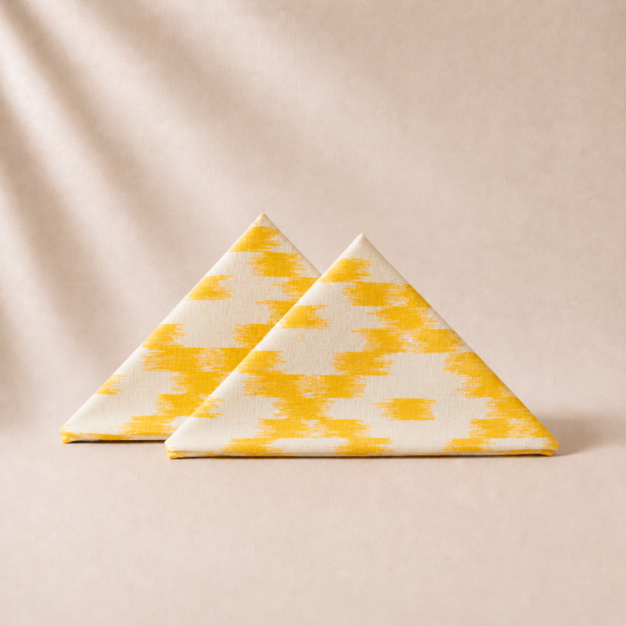Two triangular napkins with yellow and white pattern on a beige background