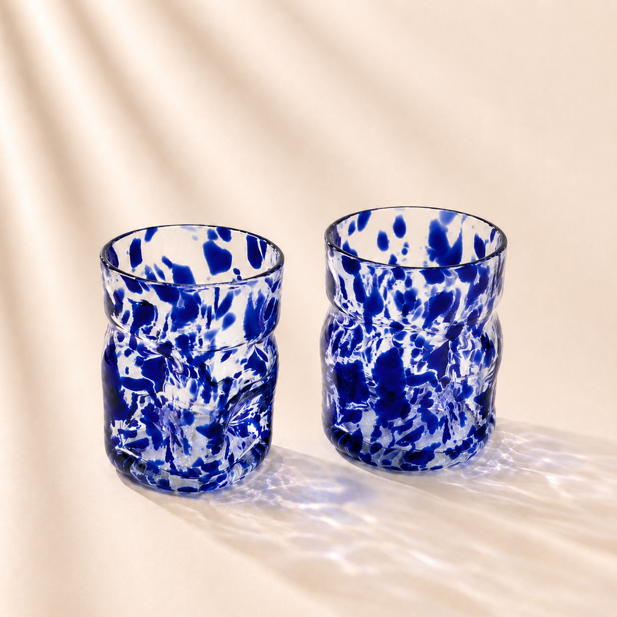 Two blue and white marbled glass tumblers on a beige background