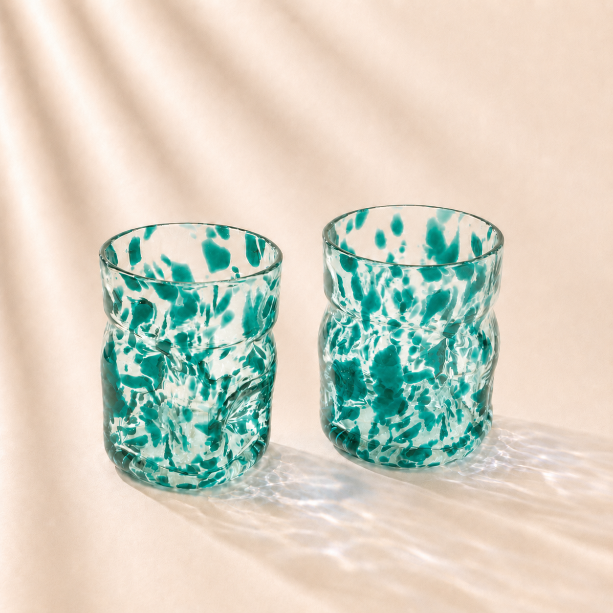 Two green and white marbled glass tumblers on a beige background