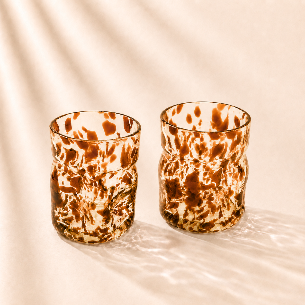 Two marbled glass tumblers on a beige background