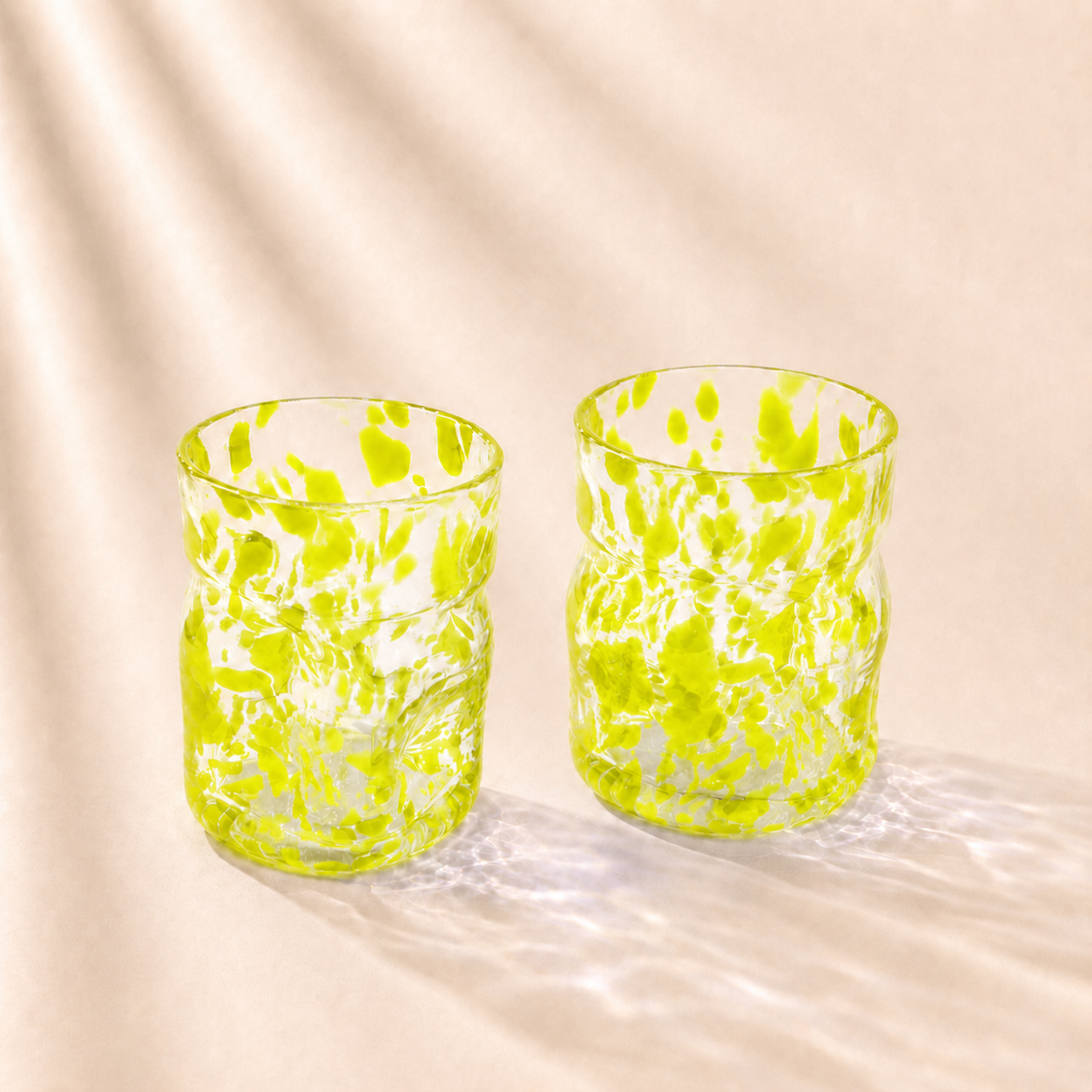 Two green glass tumblers on a beige fabric background