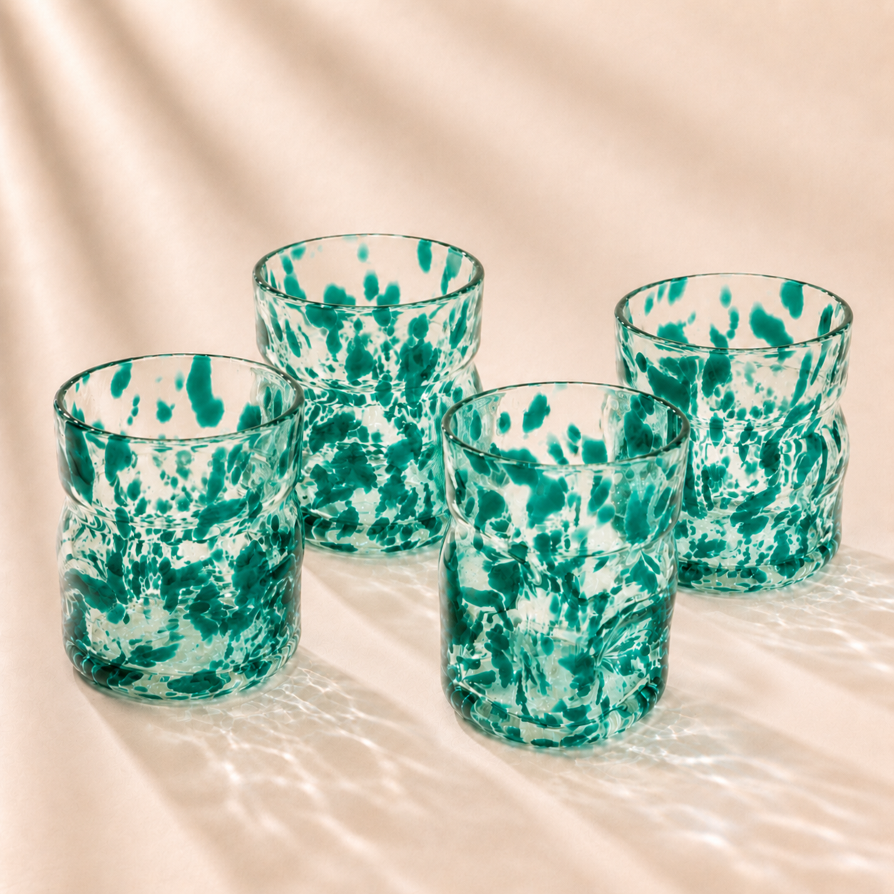 Four green deflated glasses tumblers on a beige surface