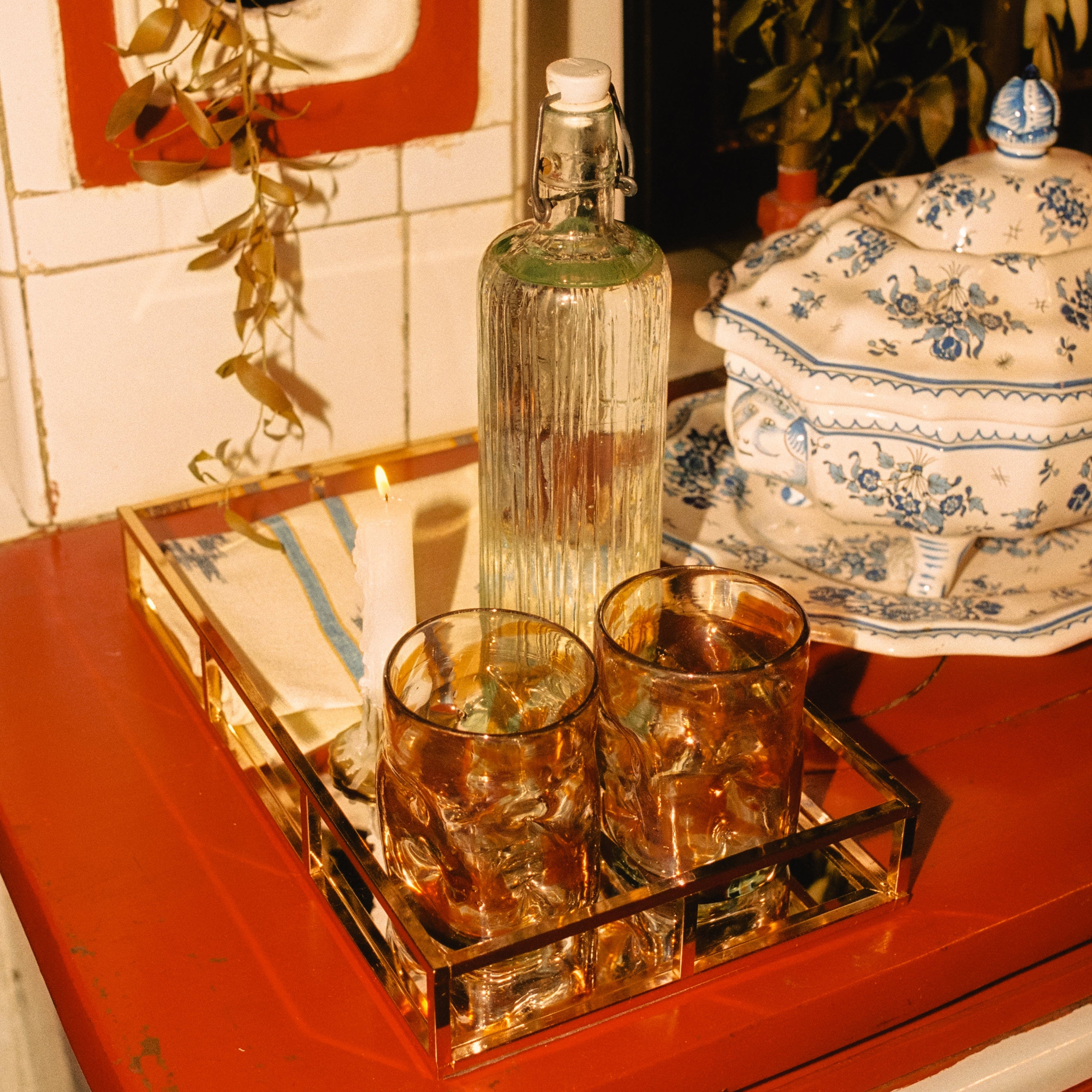 Two glasses with a bottle on a tray with a candle in the background - lifestyle
