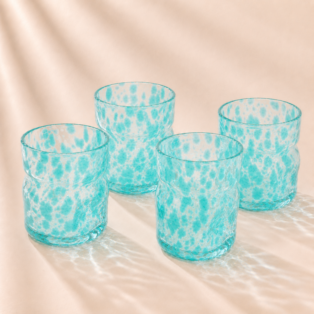 Four turquoise deflated glasses with a marbled pattern on a beige surface