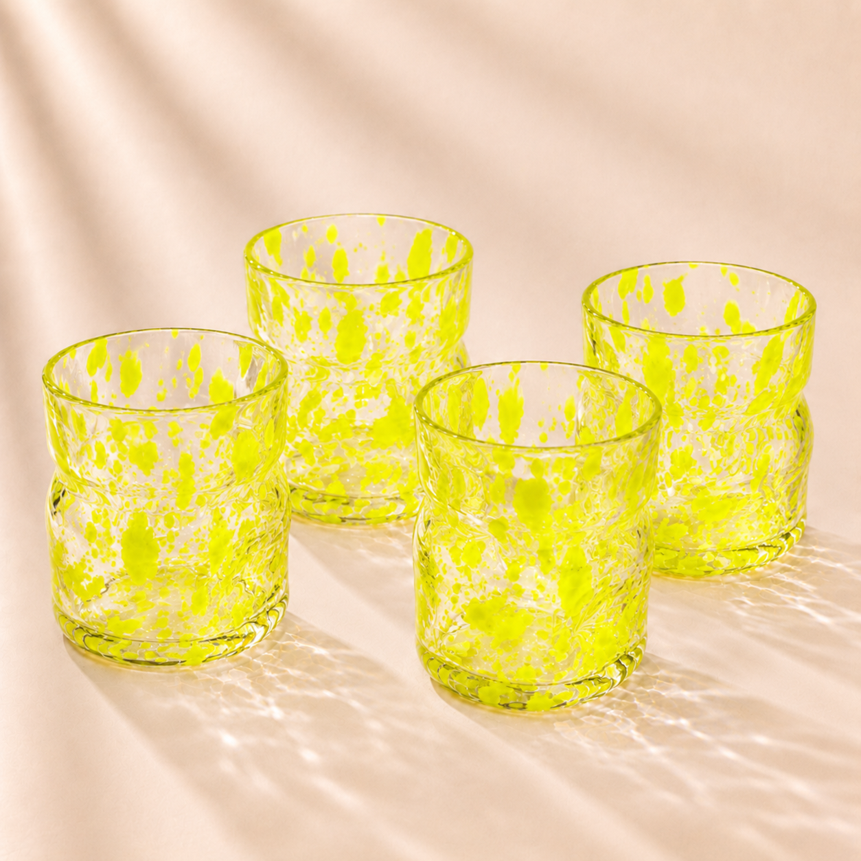 Four green deflated glasses with a speckled pattern on a beige background