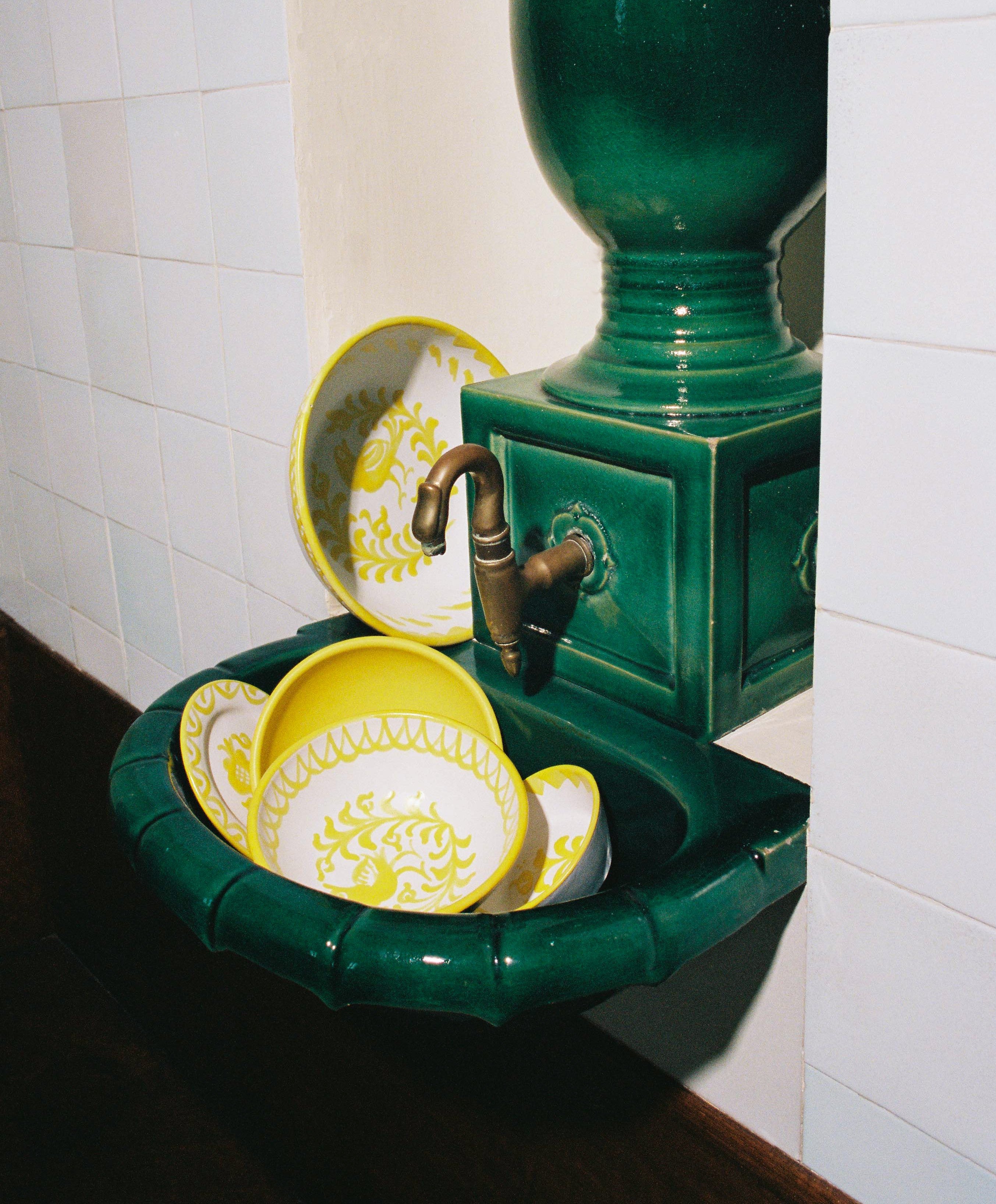 Handmade yellow ceramic tableware from Casa Maricruz placed inside a deep green ceramic sink, featuring traditional Granada-inspired motifs and Mediterranean craftsmanship.