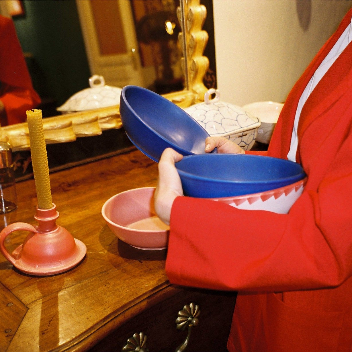 Person in a red outfit holding blue bowls in an indoor setting with a mirror and table visible.