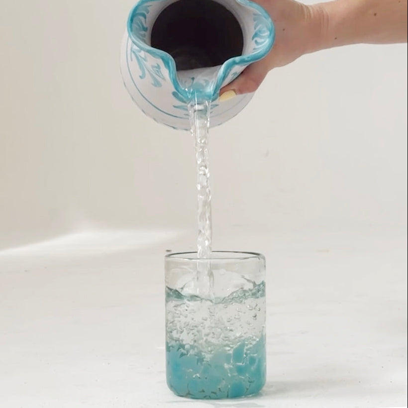 Person pouring blue liquid from a container into a glass on a white background