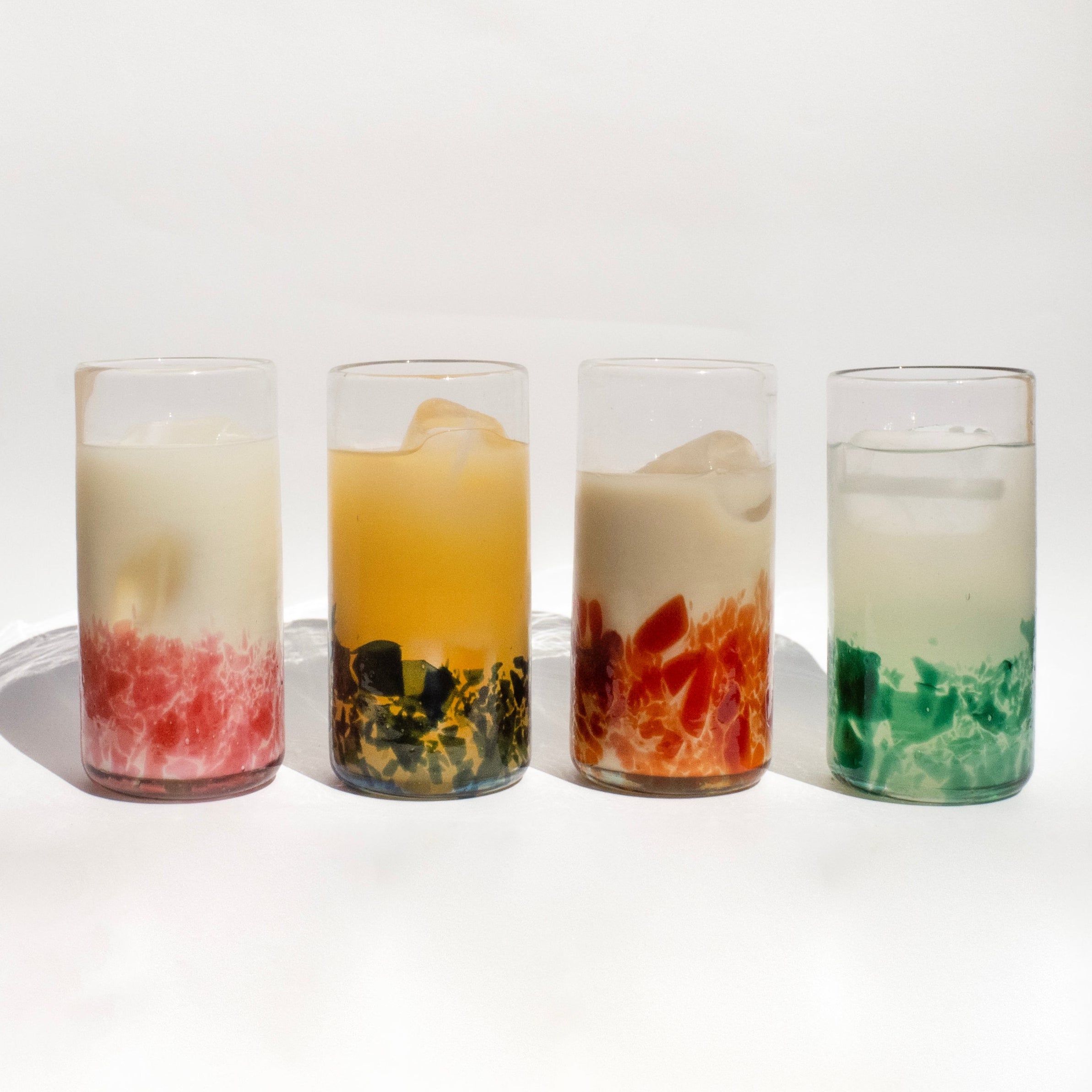 Four glasses with colorful layered drinks on a white background - lifestyle