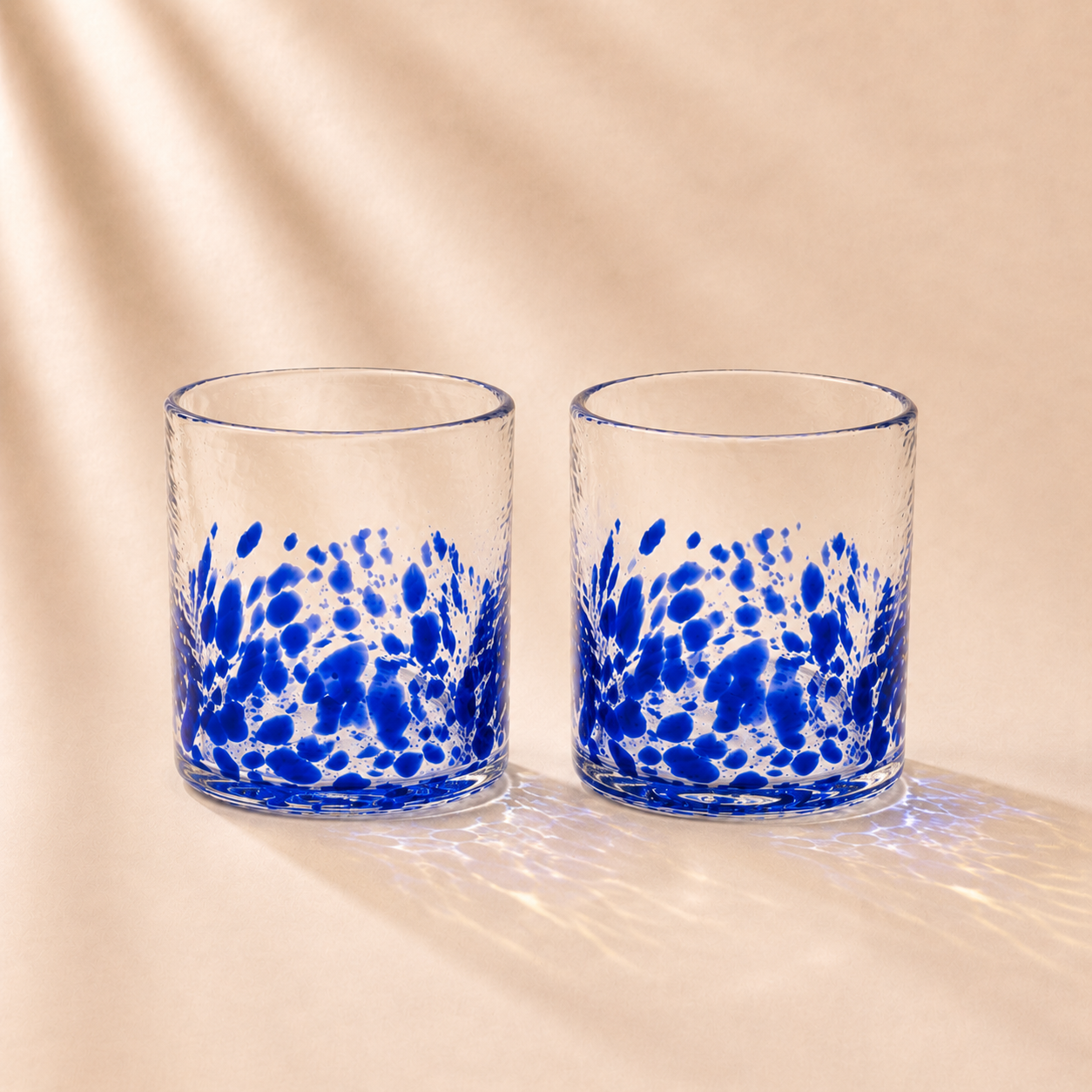 Two glass tumblers with blue abstract patterns on a beige background