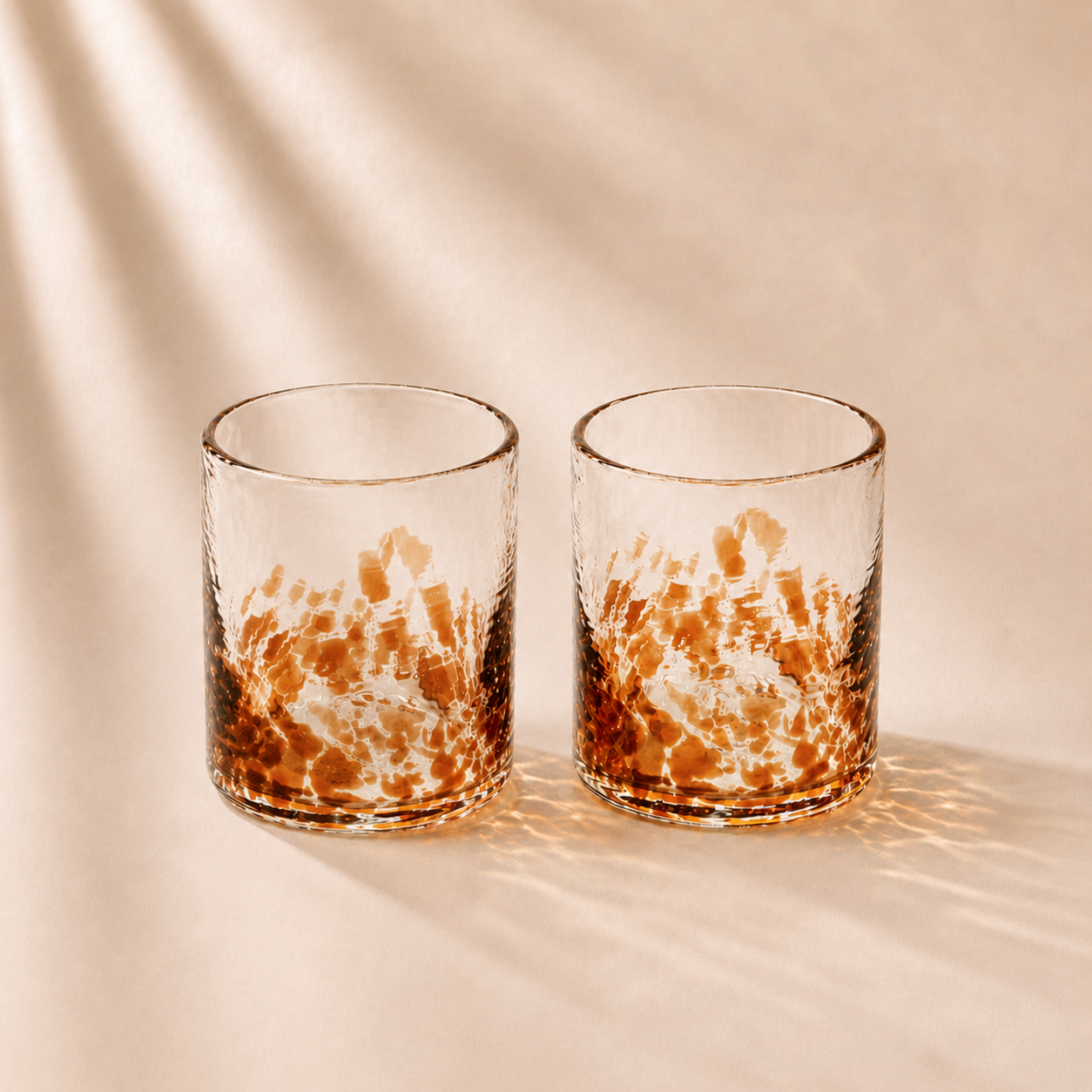 Two glass tumblers with a marbled design on a beige background