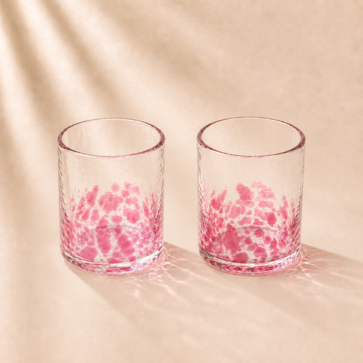 Two glass tumblers with pink interior patterns on a beige background