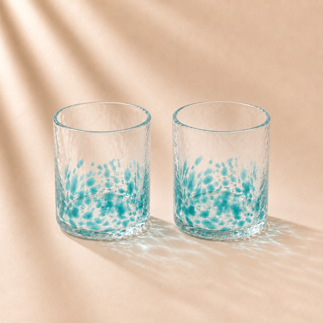 Two glass tumblers with blue speckled design on a beige background
