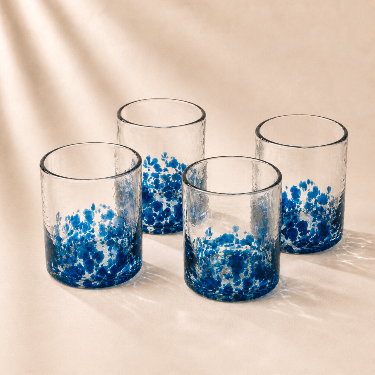 Four glass tumblers with blue and white speckled design on a beige background