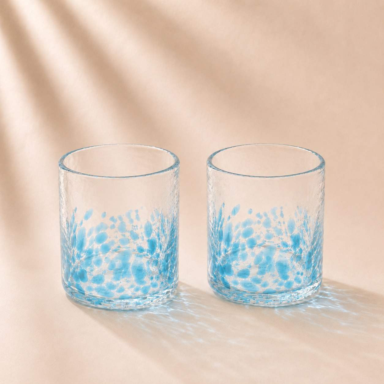 Two glass tumblers with blue abstract patterns on a beige background