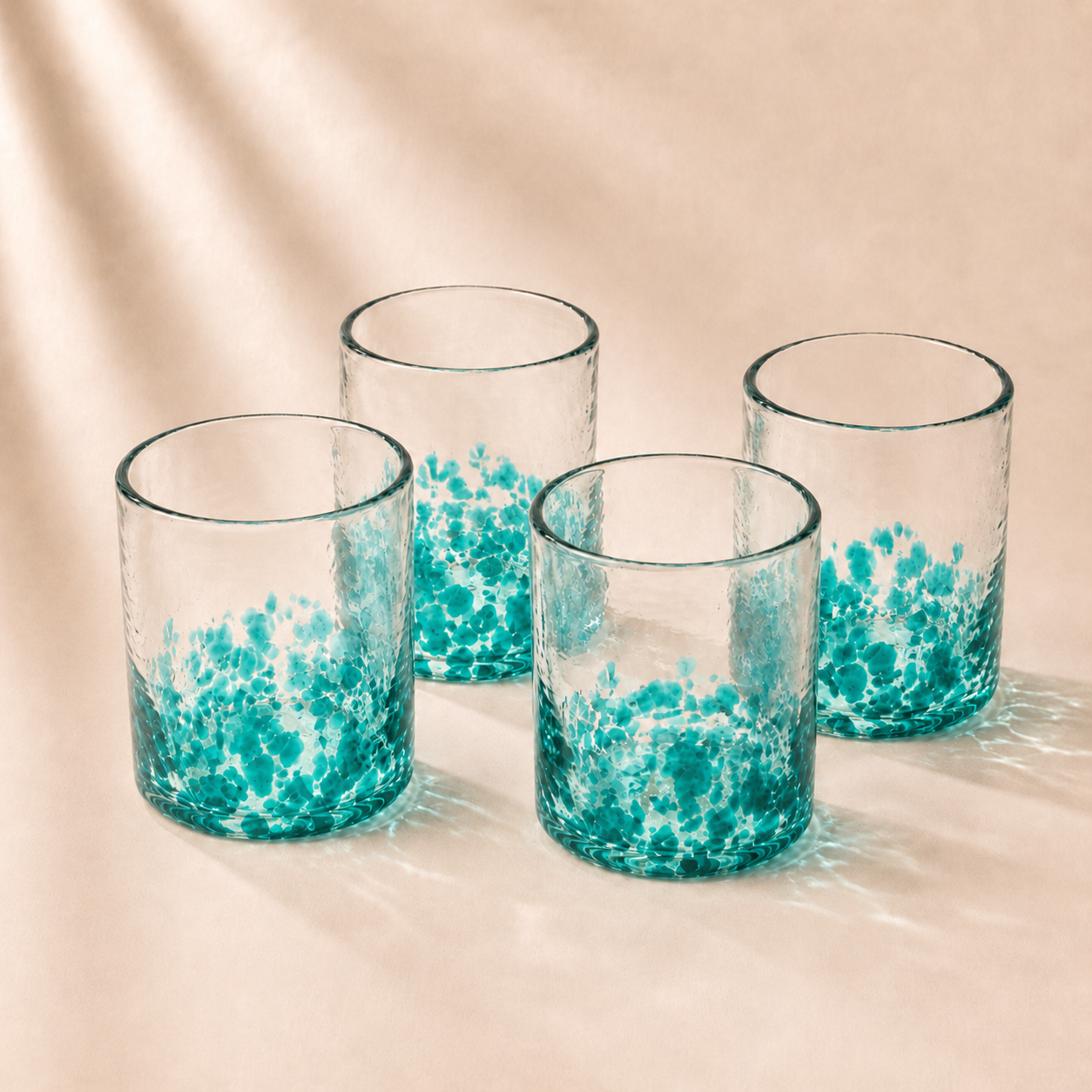 Four glass tumblers with blue speckled design on a beige background