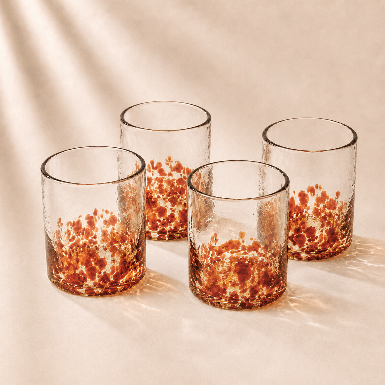 Four glass tumblers with speckled designs on a beige background