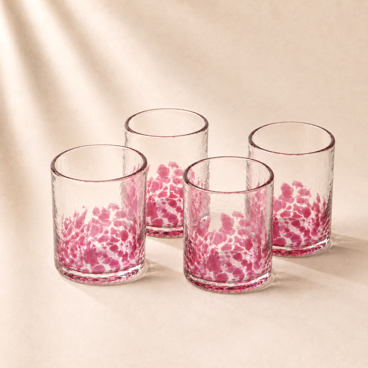 Set of four glass tumblers with pink marble pattern on a beige background