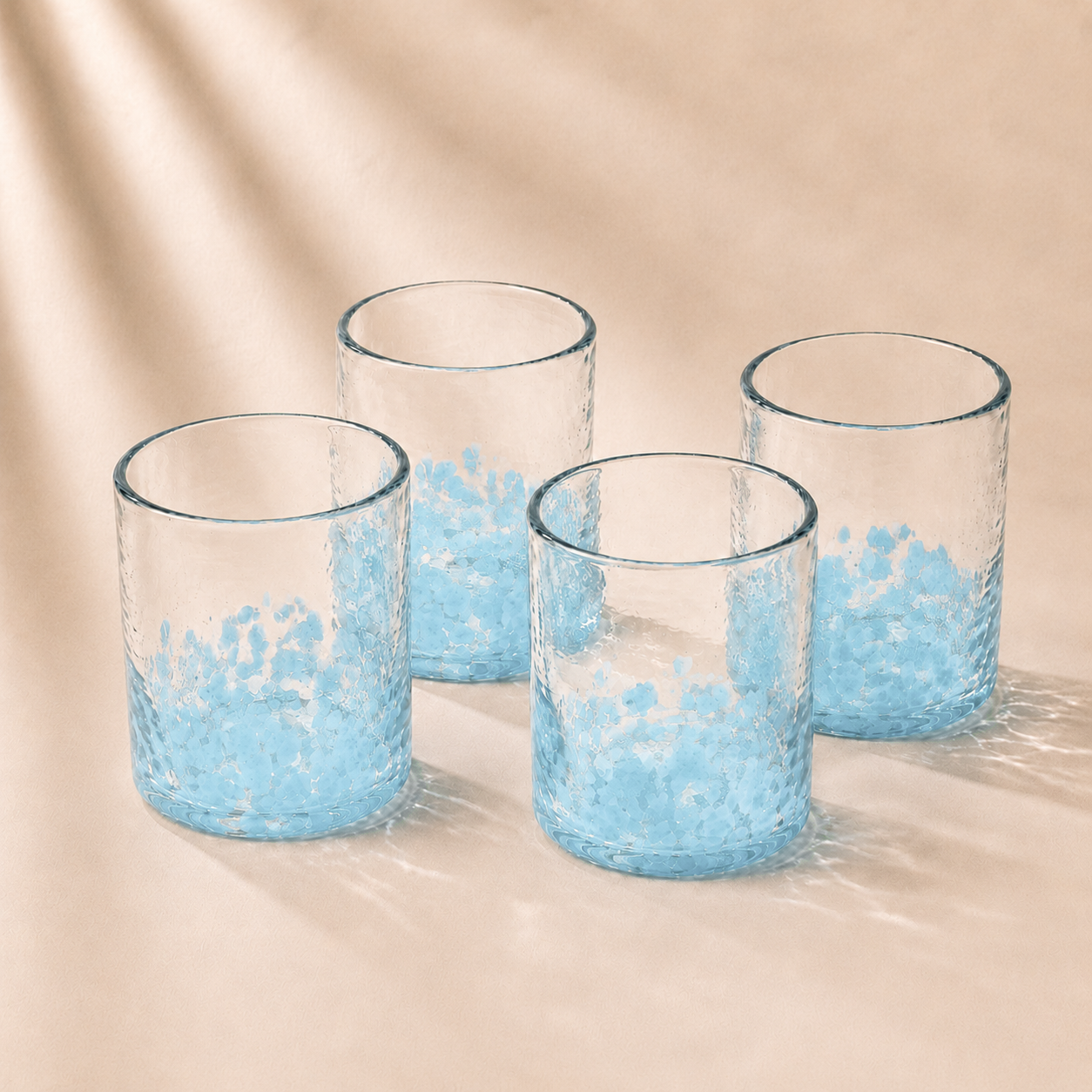 Four clear glasses with blue speckled designs on a beige background