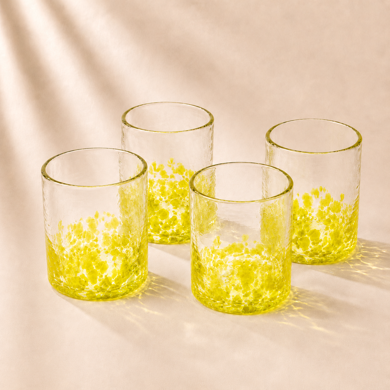 Four clear glass tumblers with yellow interior and base on a beige background