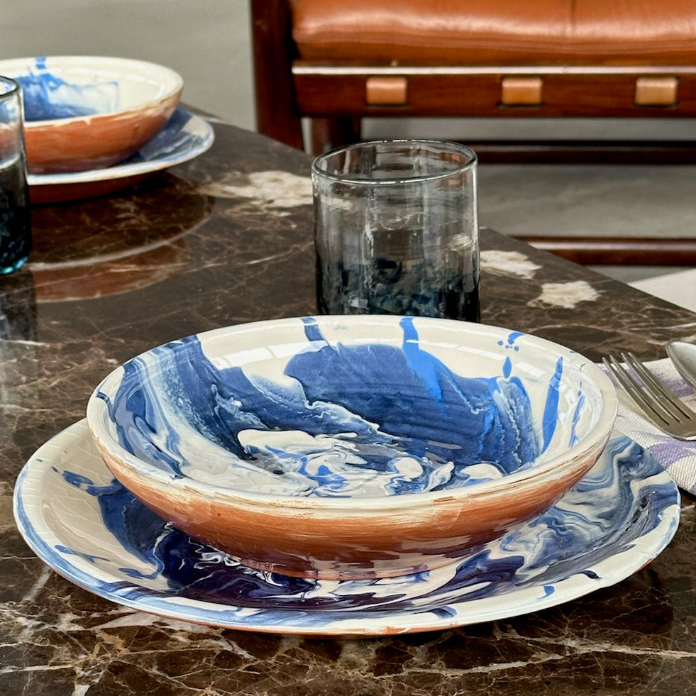 Blue and brown marbled ceramic plates on a marble table with a glass of water.