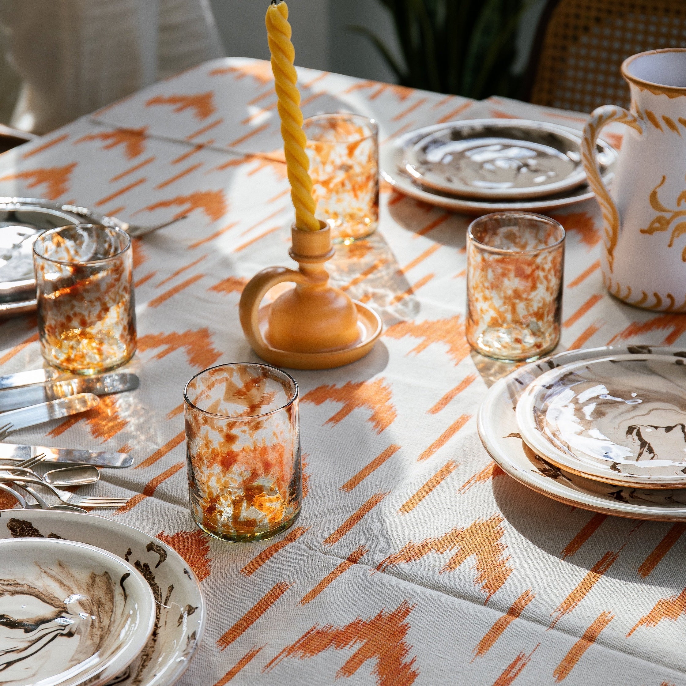 Dining table setting with patterned tablecloth, glasses, and ceramic items. - lifestyle