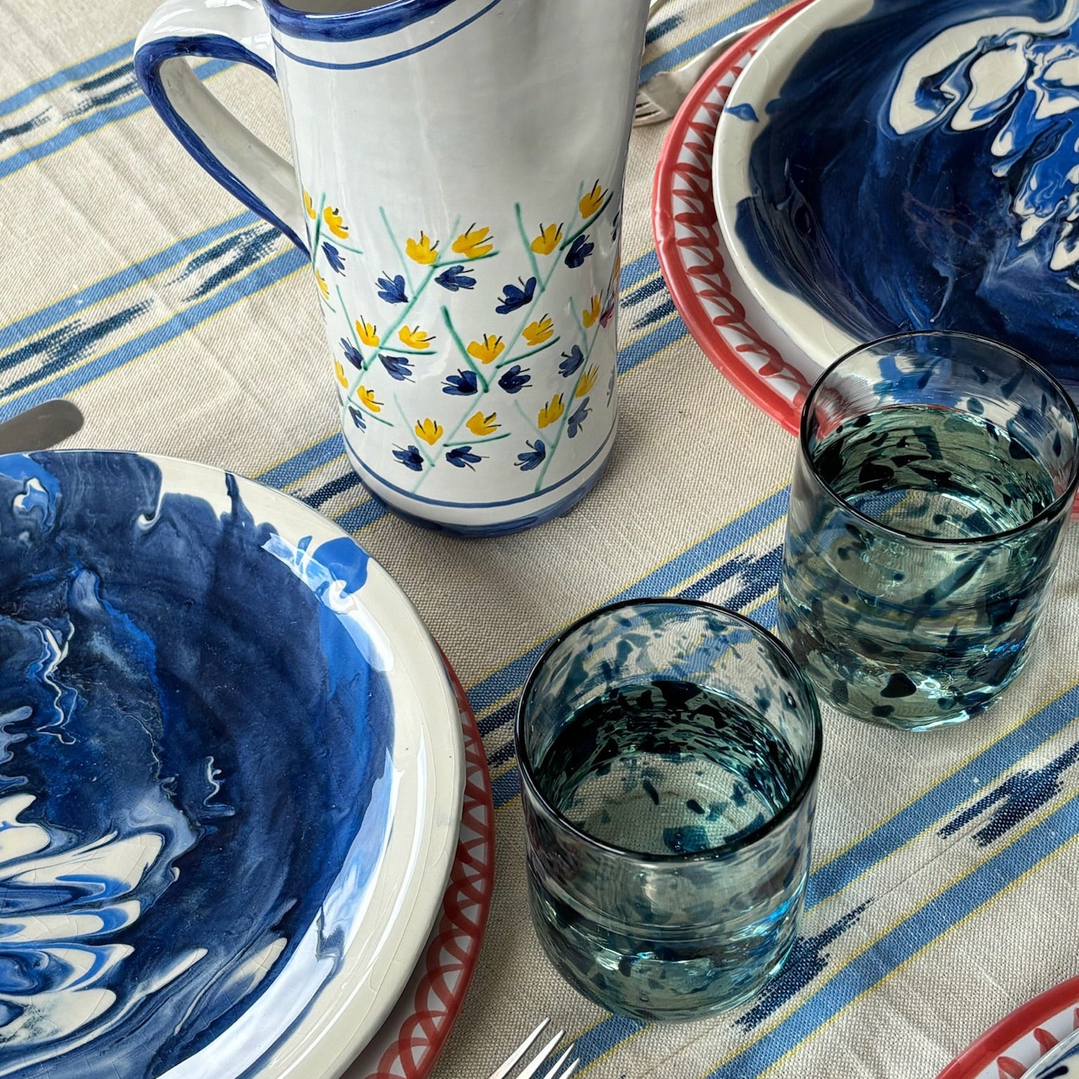 Ceramic pitcher and bowls with blue and yellow patterns on a tablecloth with blue and white stripes. - lifestyle