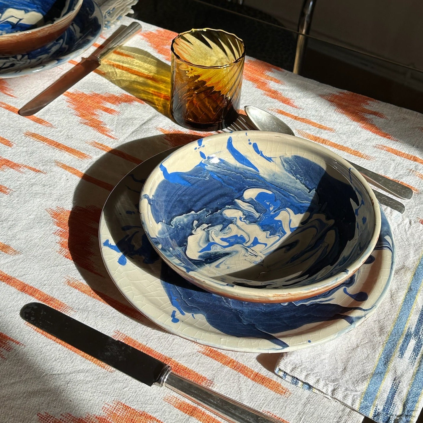 Dining table setting with blue and white ceramic plates on a patterned tablecloth.