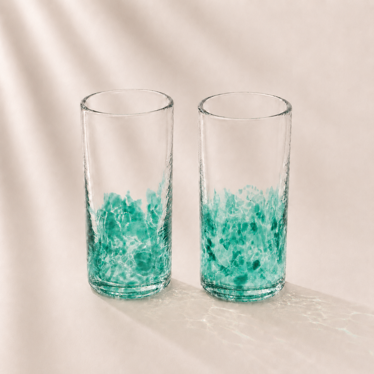 Two clear glasses with green marbled design on a beige background