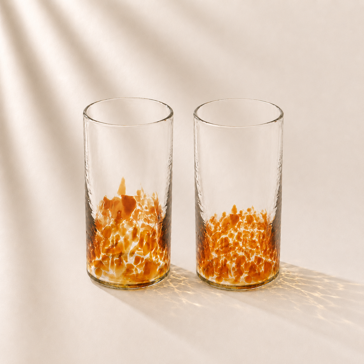 Two clear glasses with orange interior patterns on a beige background