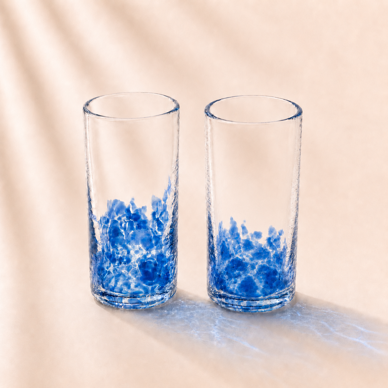 Two clear glasses with blue ocean wave design on a beige background