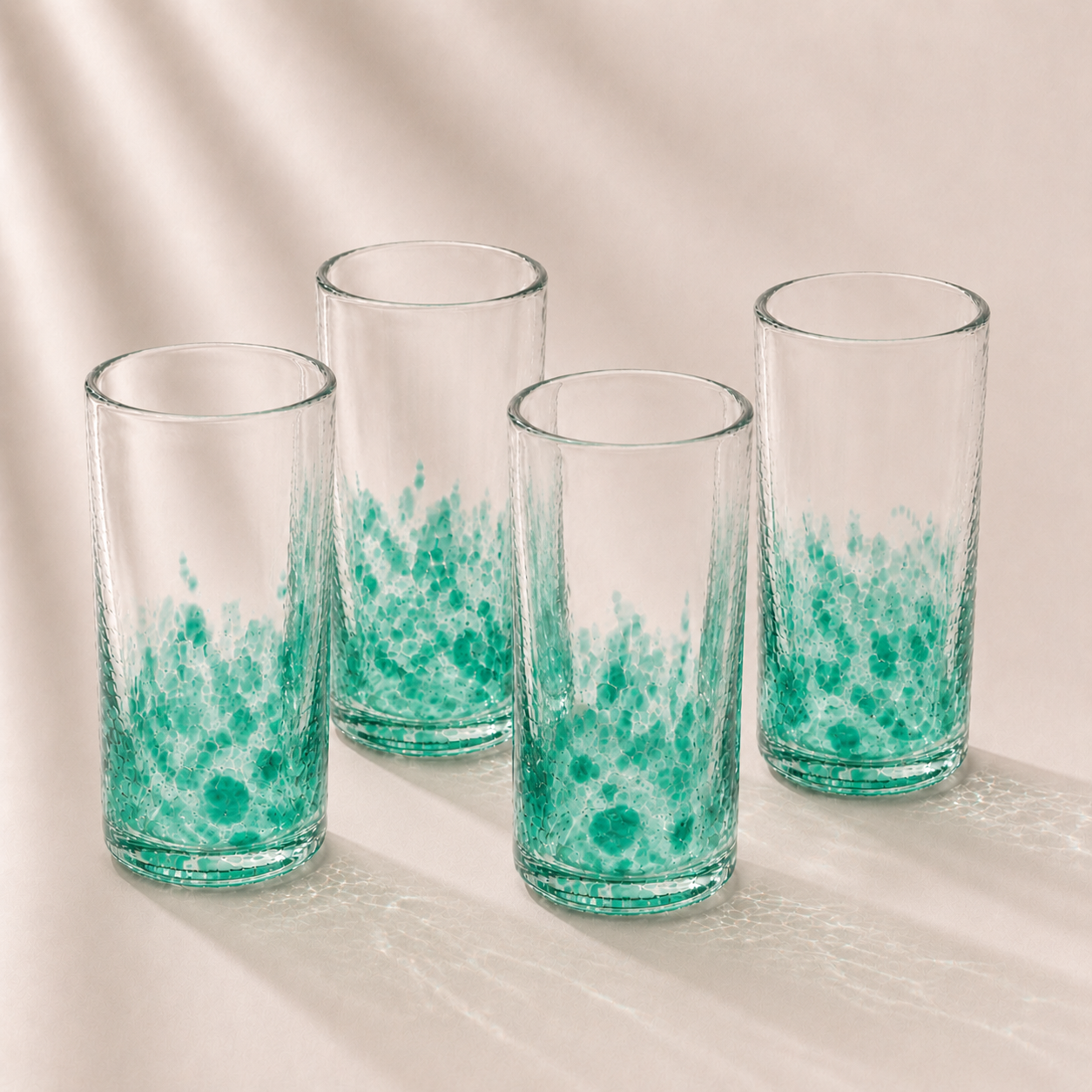Four clear glasses with green marbled design on a beige background