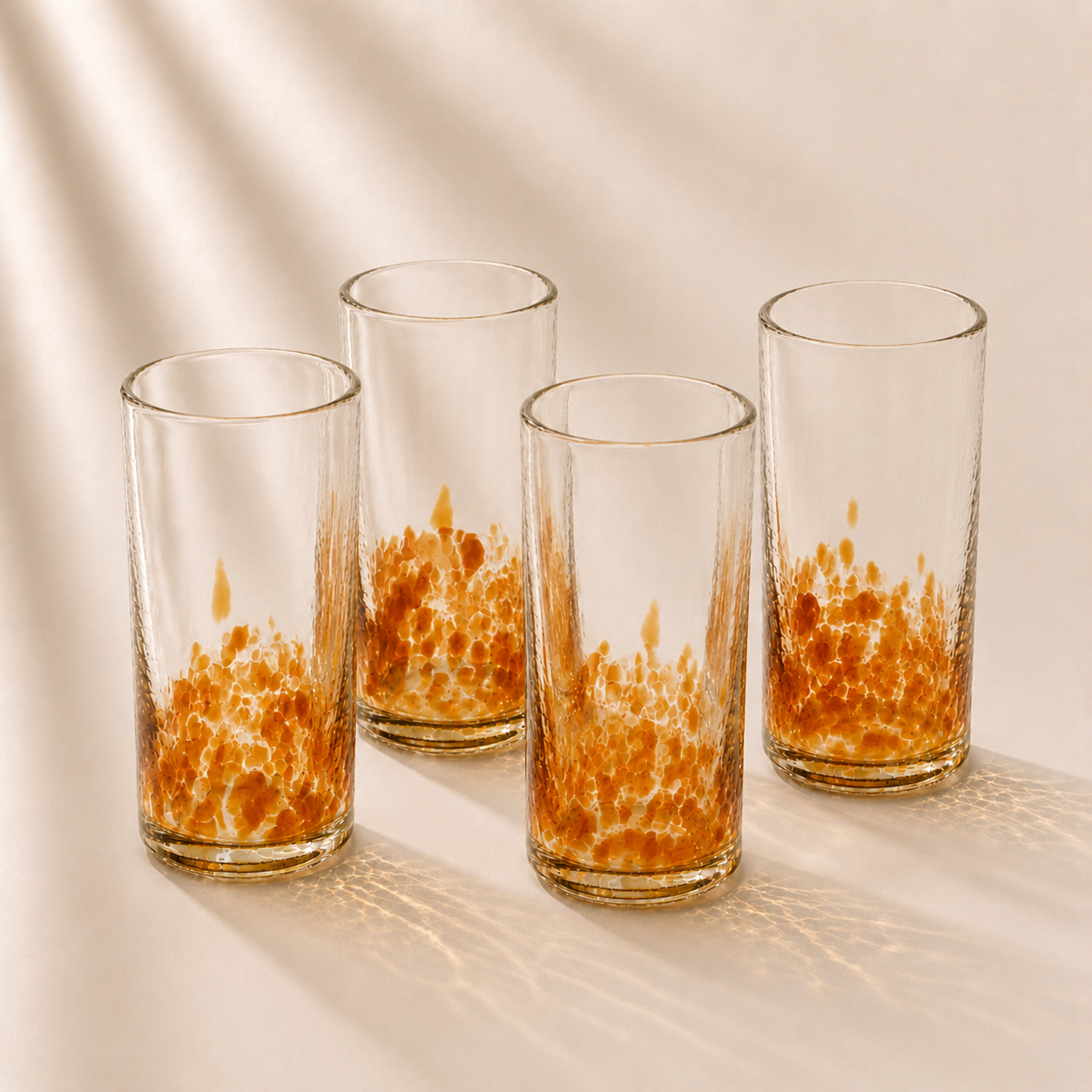 Four glass tumblers with orange speckled designs on a beige background