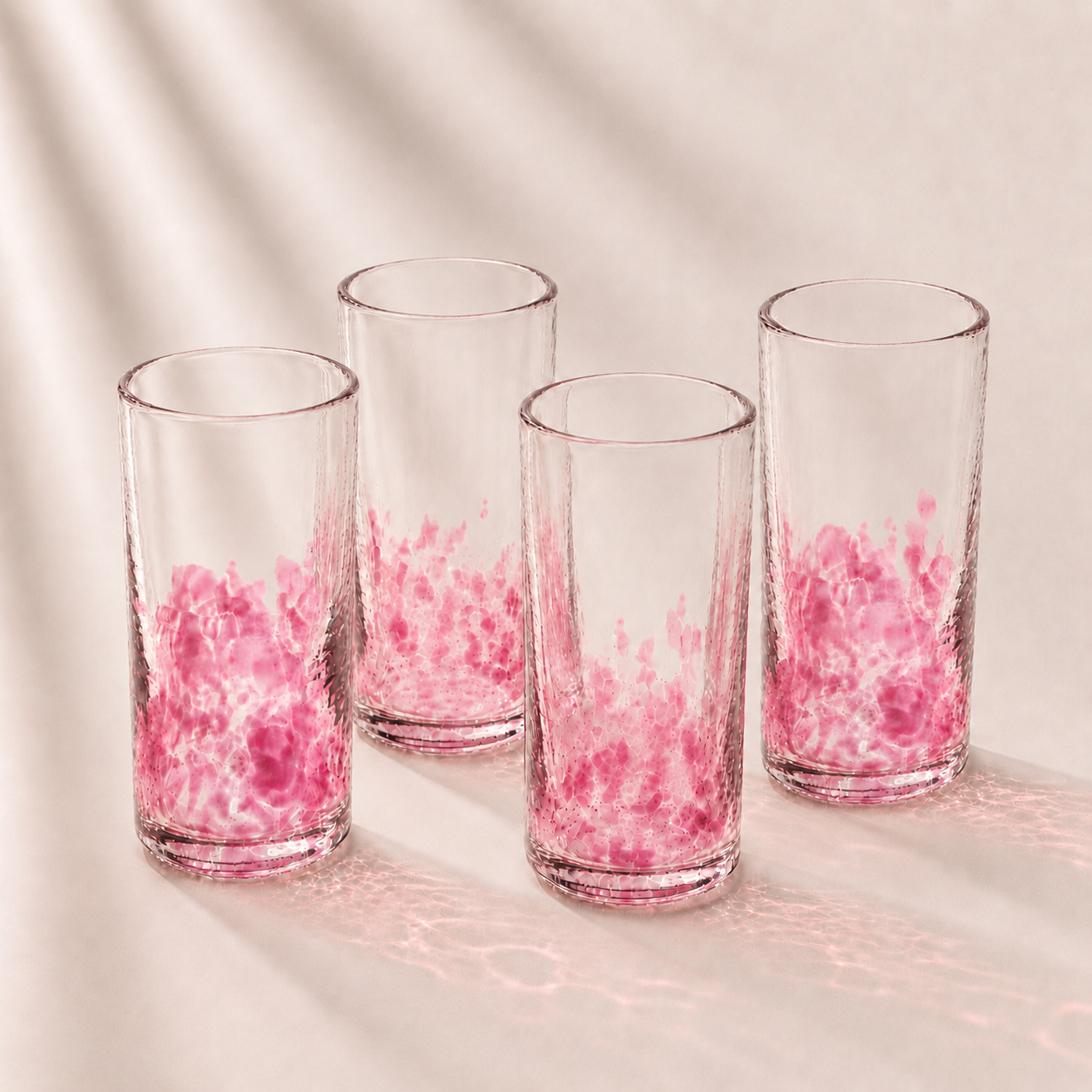 Four clear glasses with pink interior patterns on a light background