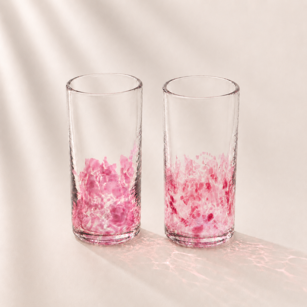 Two clear glasses with pink marbled design on a light background