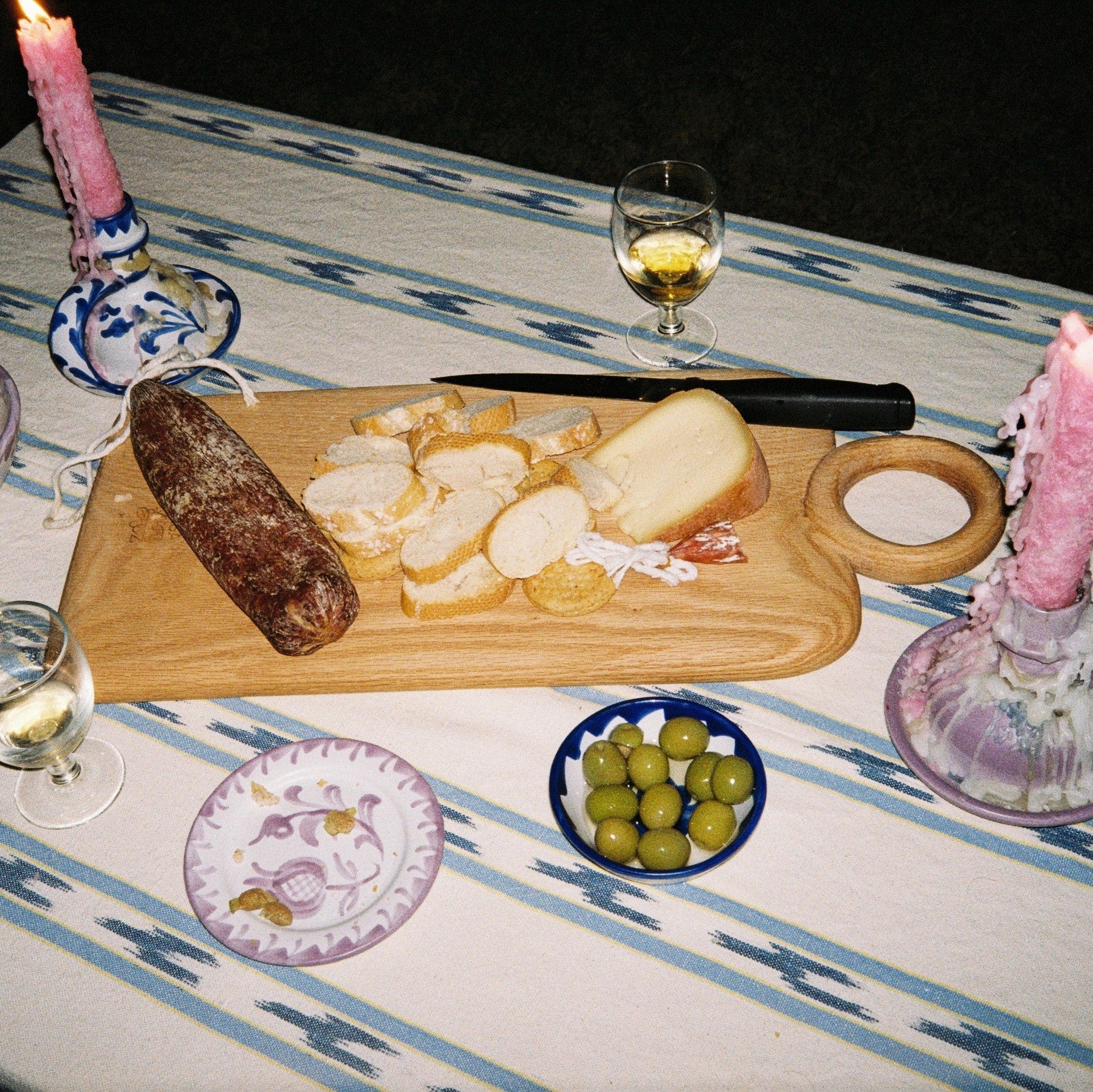 Table setting with a charcuterie board, candles, and wine glasses on a striped tablecloth. - lifestyle
