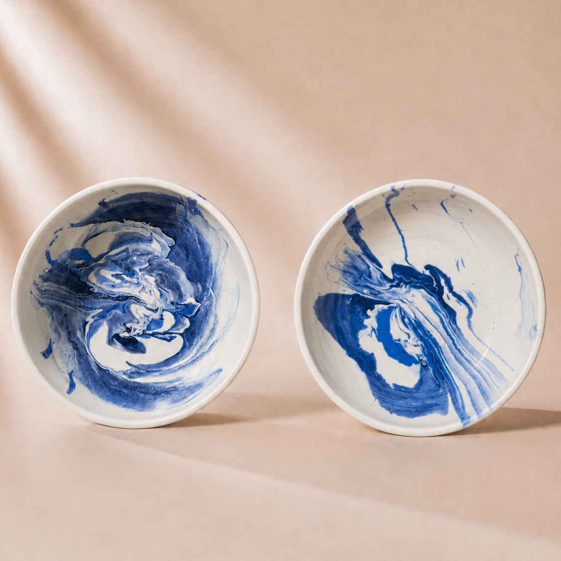 Two ceramic bowls with blue and white marbled design on a beige background